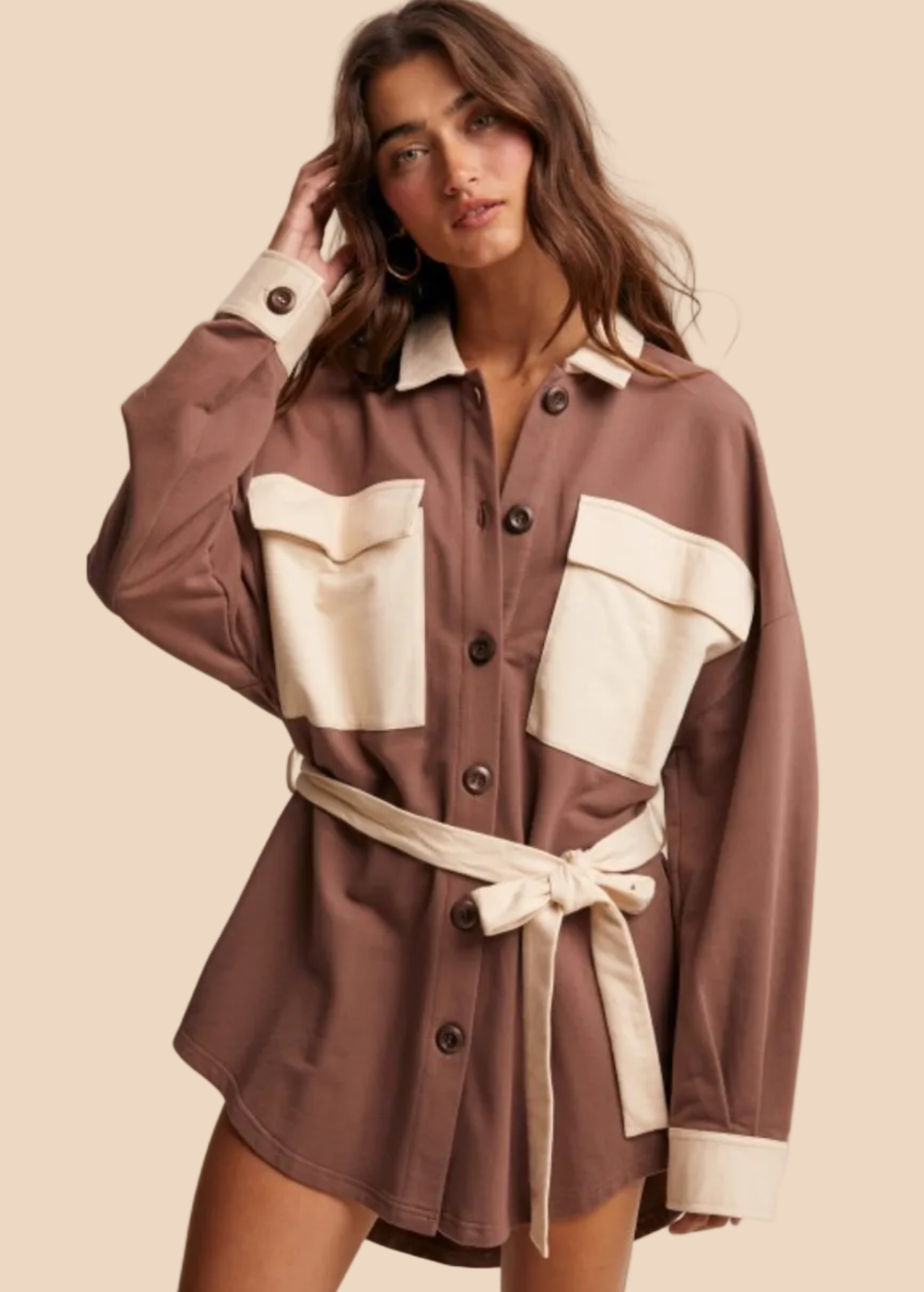 Woman wearing a brown and beige jacket with a belt on a beige background, displayed on the Listicle app.